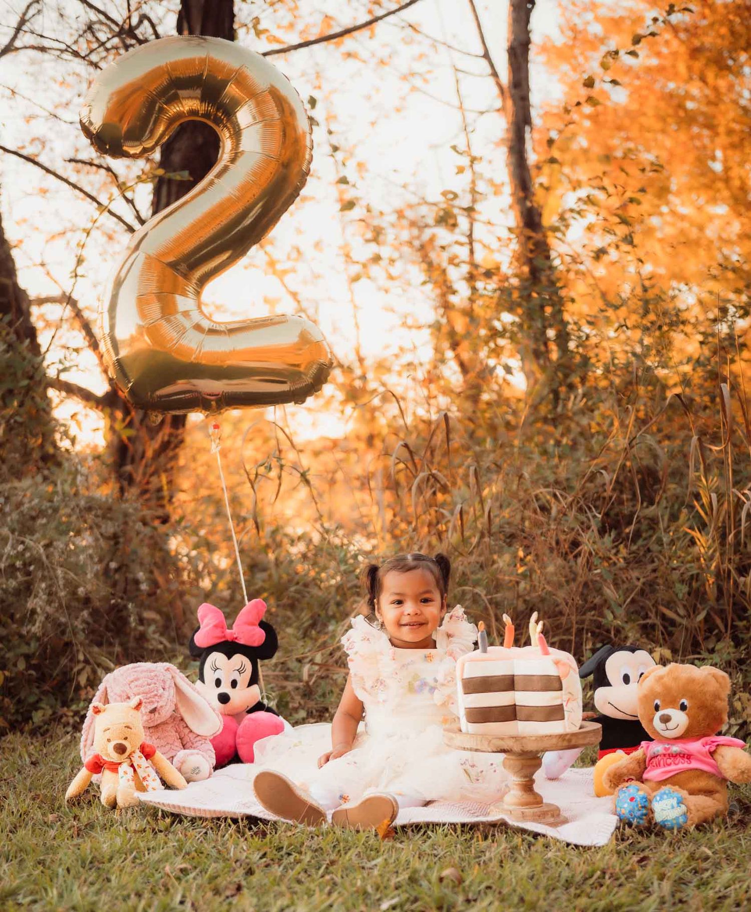 A baby milestone photo series showing growth from one to two years old with pink and gold decorations in an autumn setting.