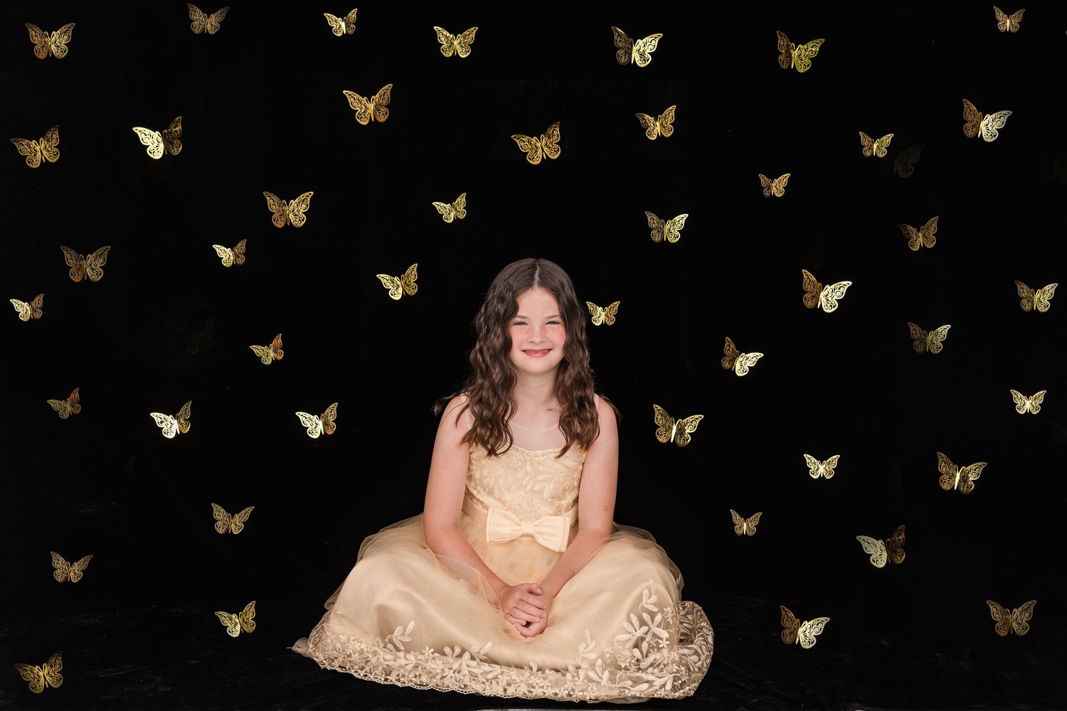 A figure in a cream-colored dress sits centered against a dark background with golden butterflies scattered throughout.