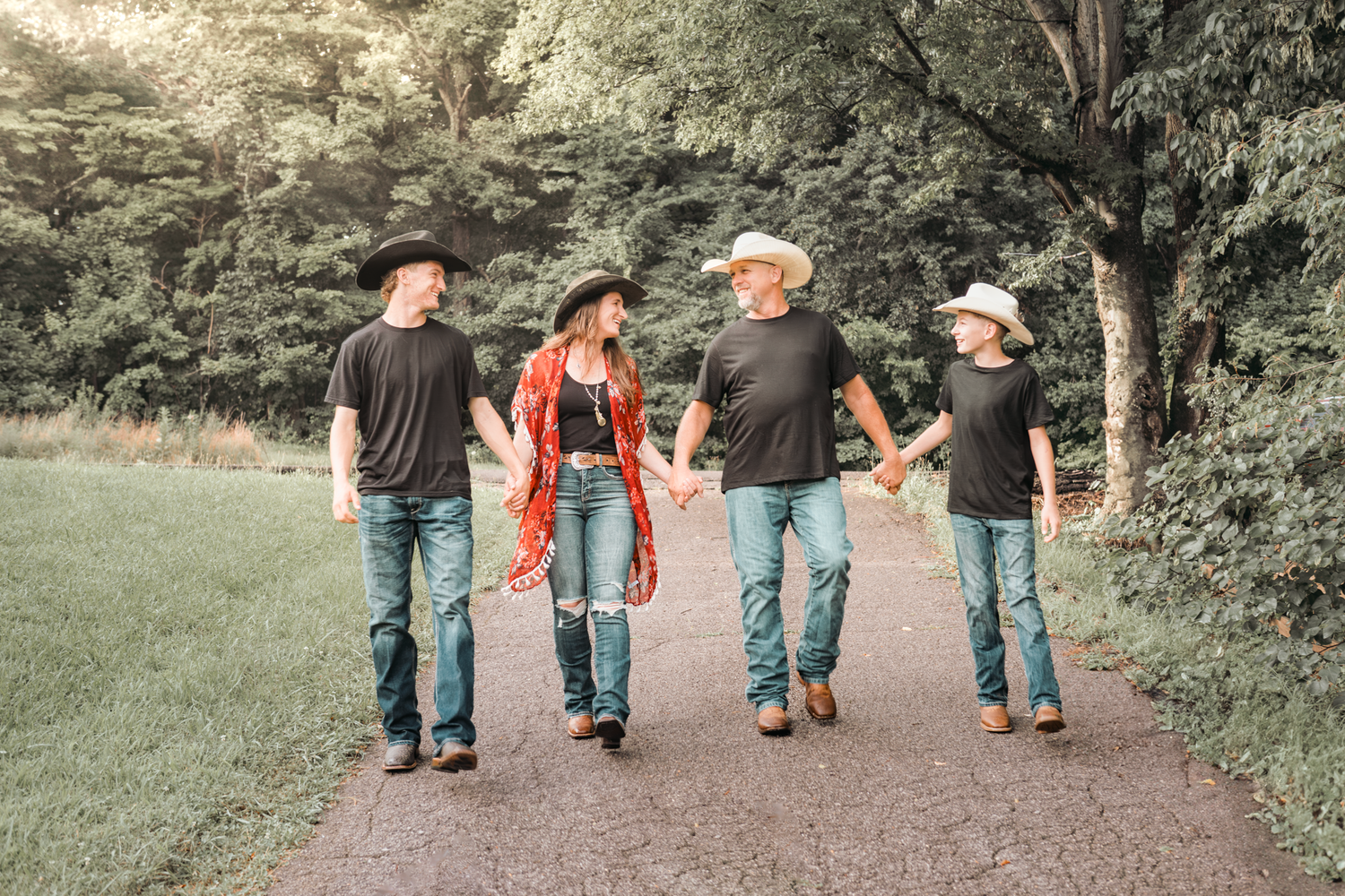 Group walking together on a trail through a lush green park, wearing casual clothing and hats on a sunny day.