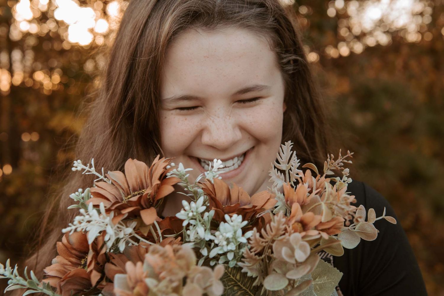 A joyful close-up portrait with autumn-colored flowers in front of a blurred orange and brown background.