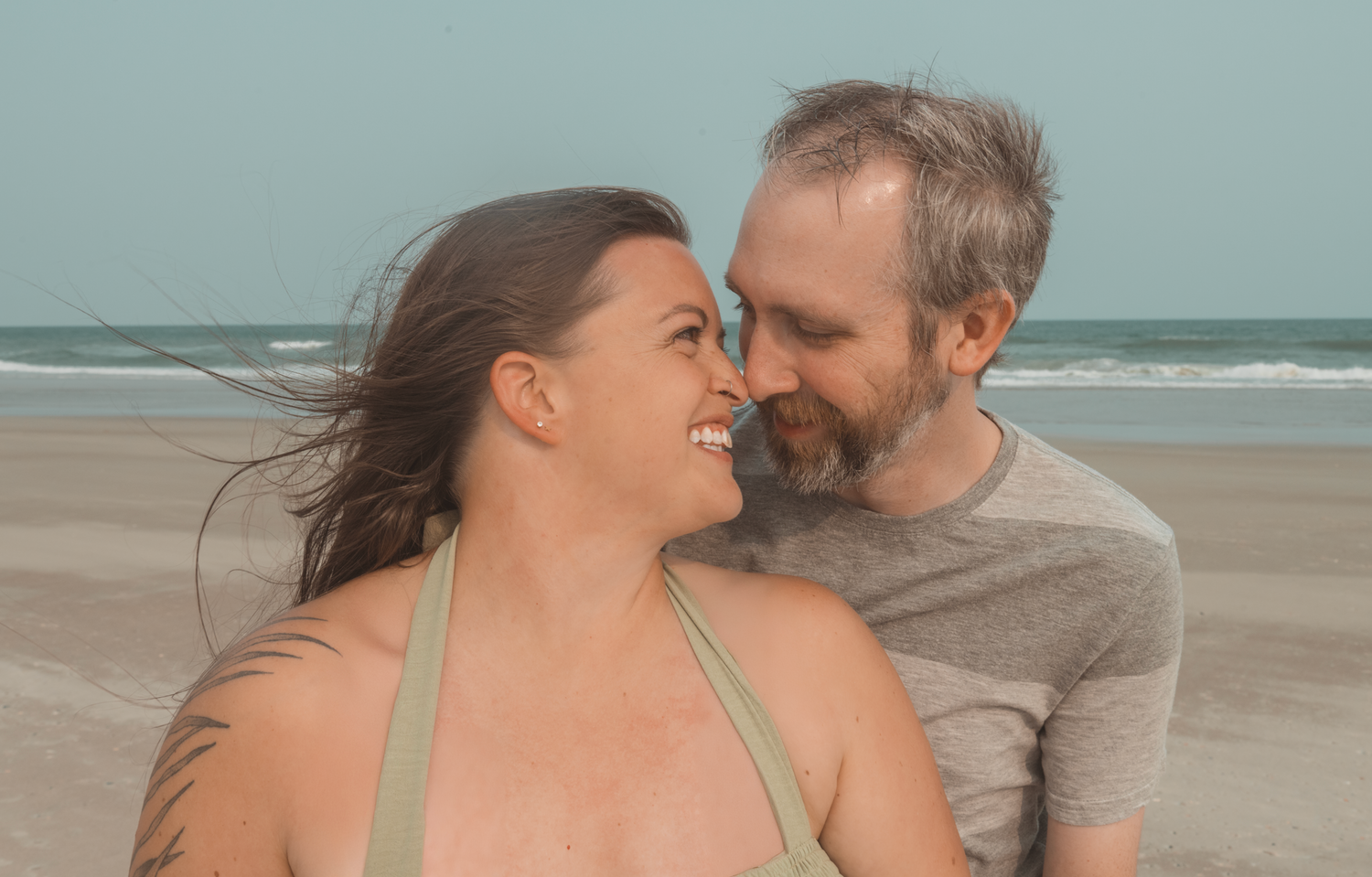 A couple enjoying a playful moment together on a serene beach with ocean waves in the background.