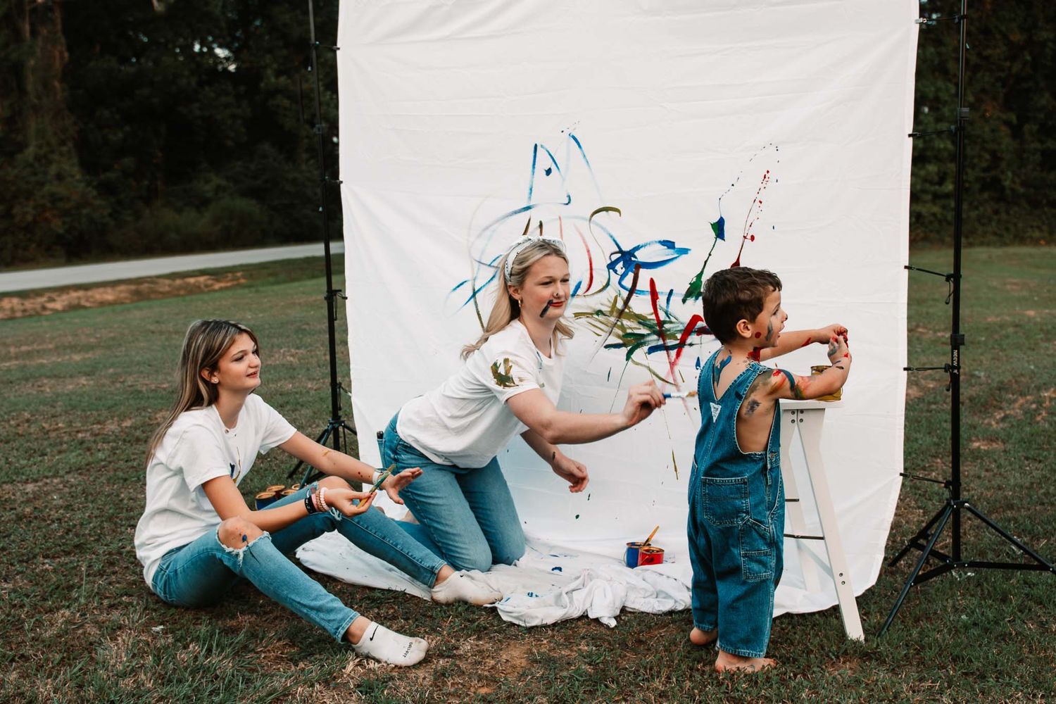 Creative family art session outdoors with paint splatters on white backdrop and participants in casual clothing.
