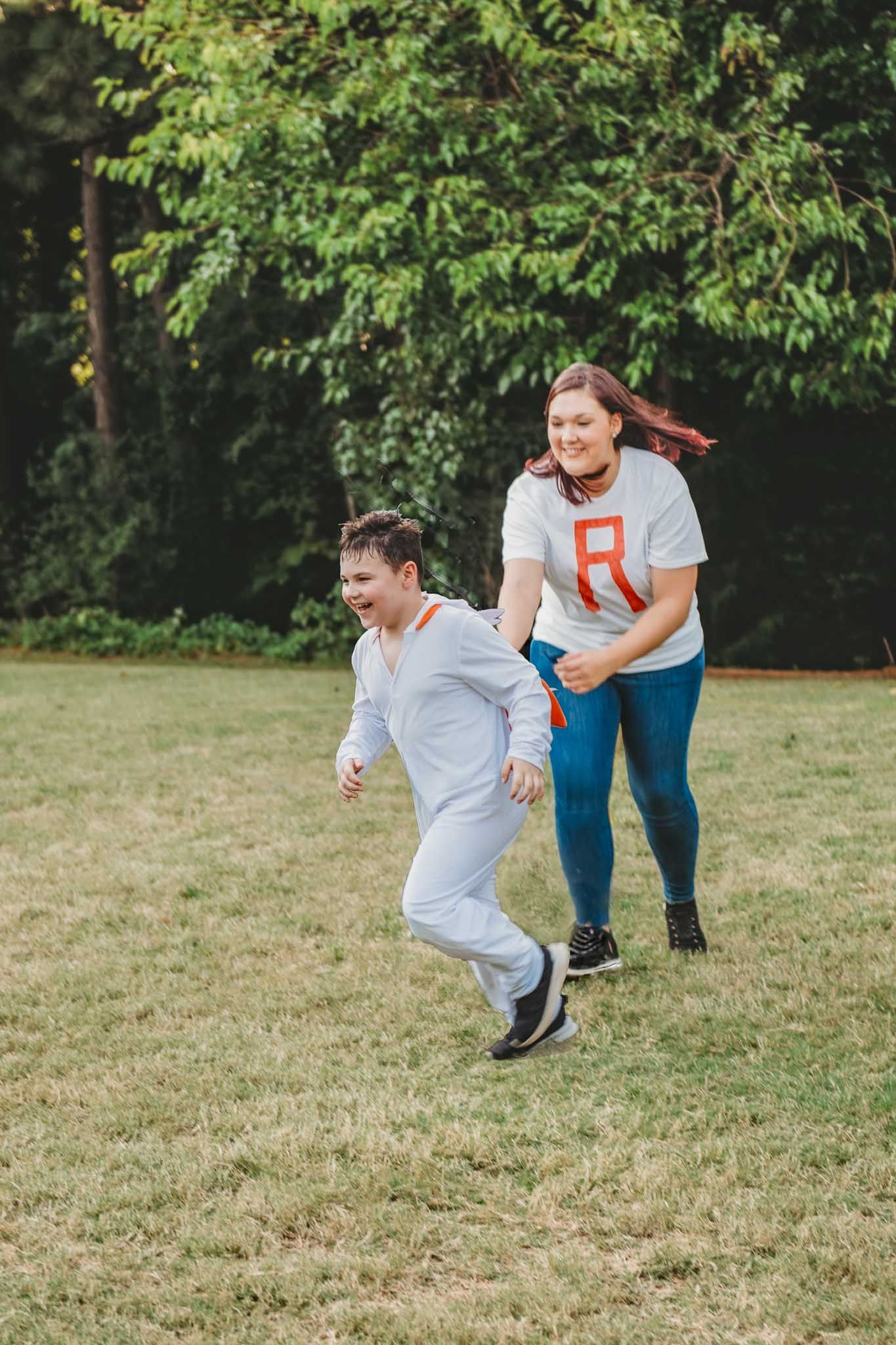 Two people running and playing together in a grassy field on a sunny day with trees in the background.