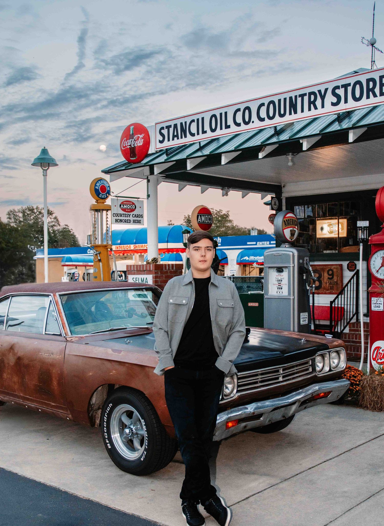 Vintage car parked at retro Stancil Oil Co Country Store gas station with classic gas pumps at sunset.