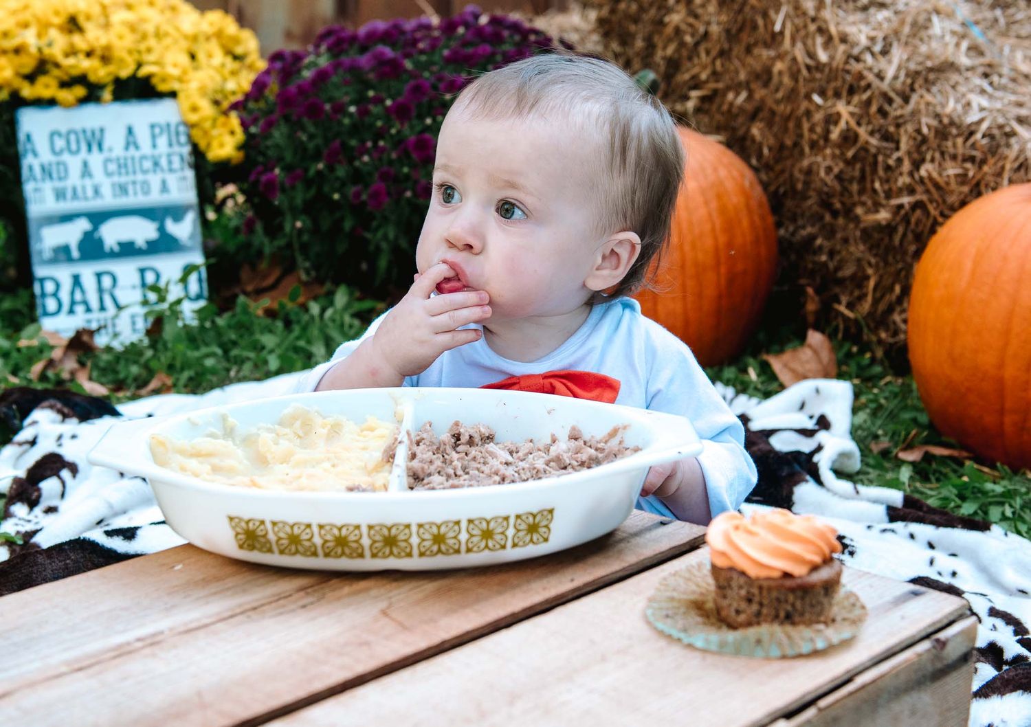 Young child sits at outdoor table with pumpkin pie and fall decorations during harvest season.