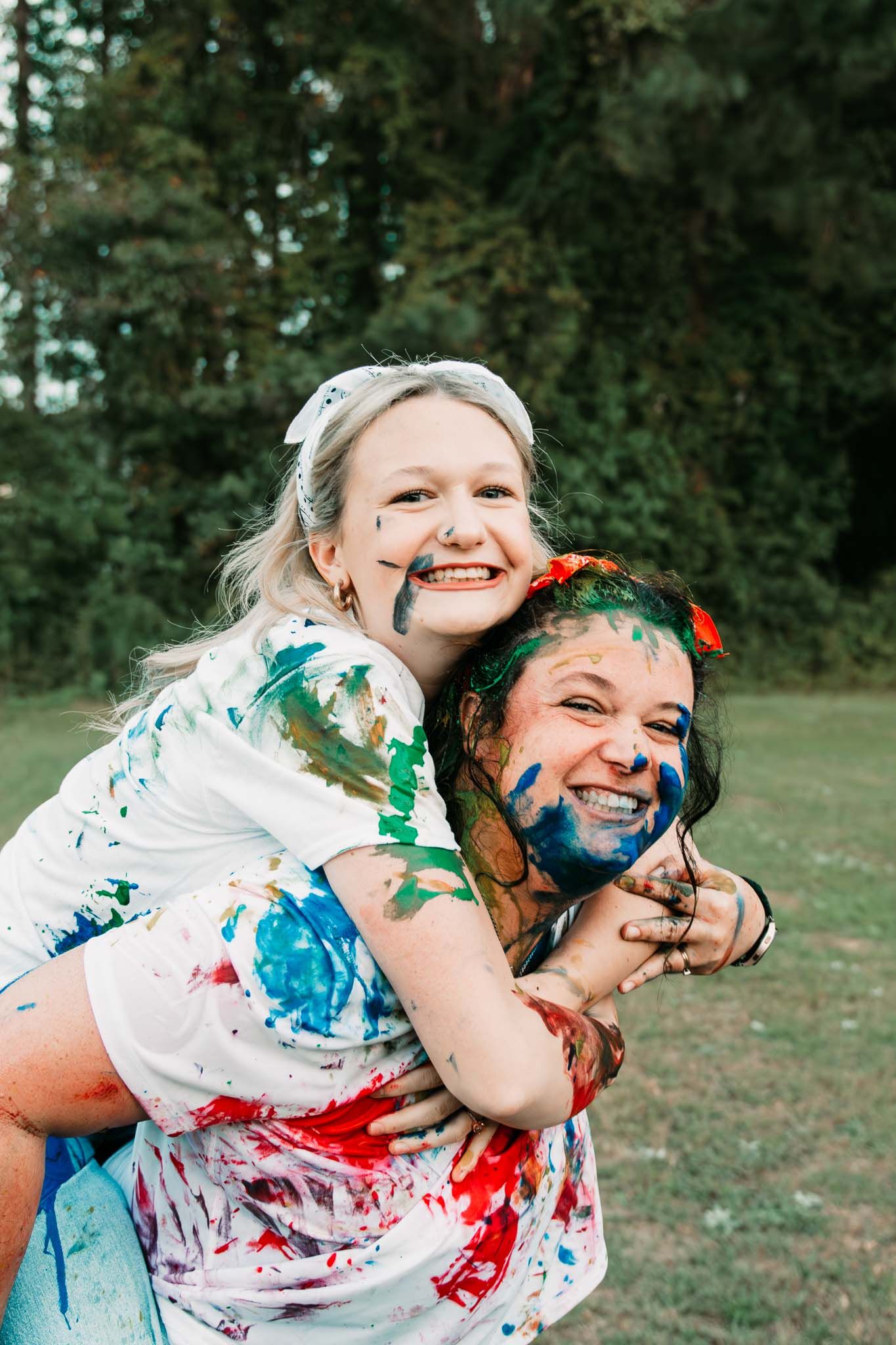 Two people covered in colorful paint and glitter have fun playing outdoors during a joyful photoshoot.