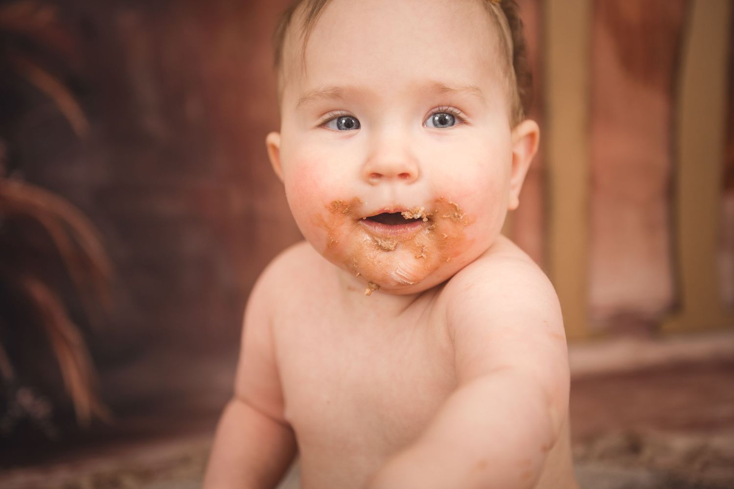A happy baby sits with chocolate smeared all over their face after enjoying a sweet treat.