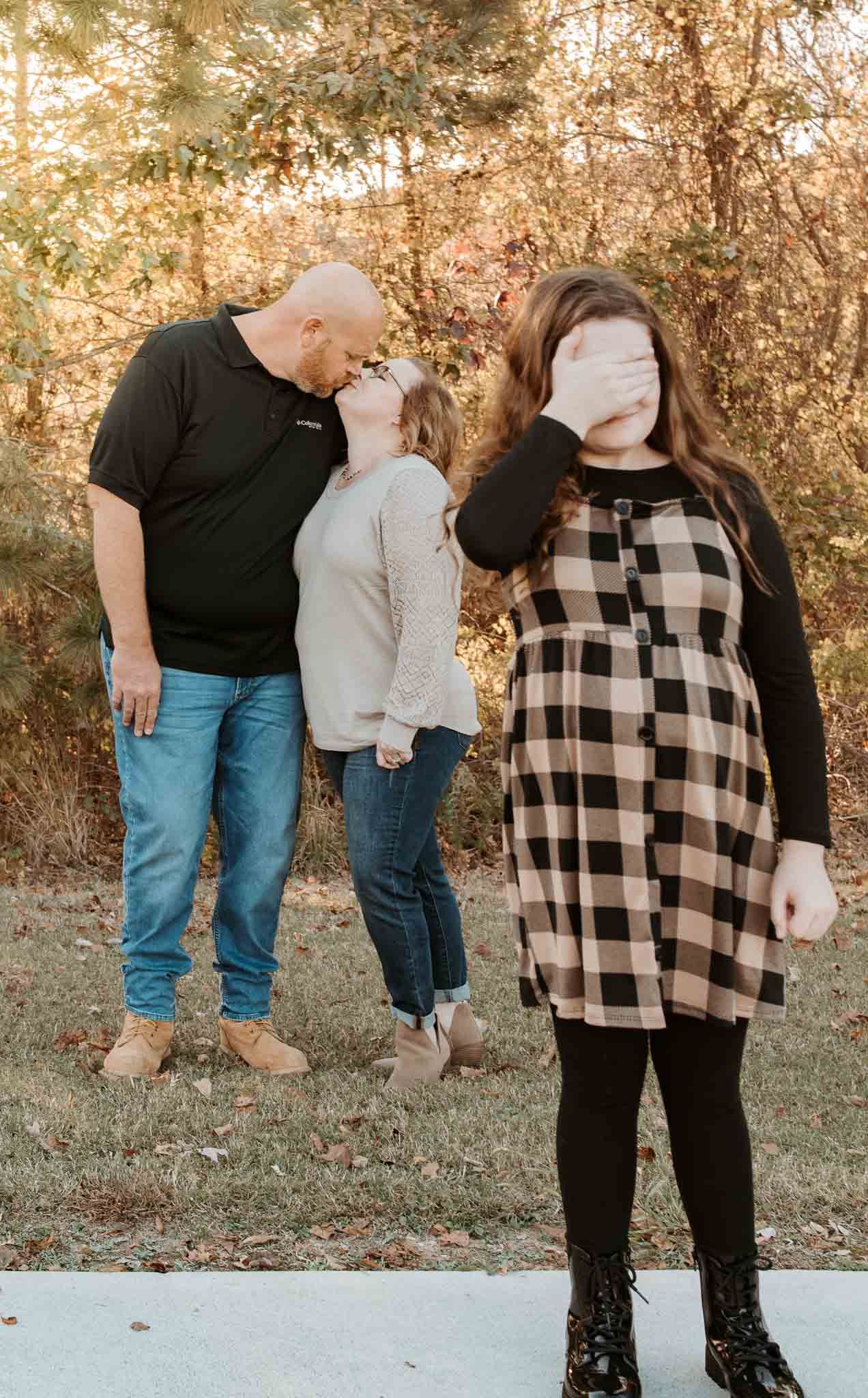 Three people pose playfully together outdoors with fall foliage in the background at sunset.