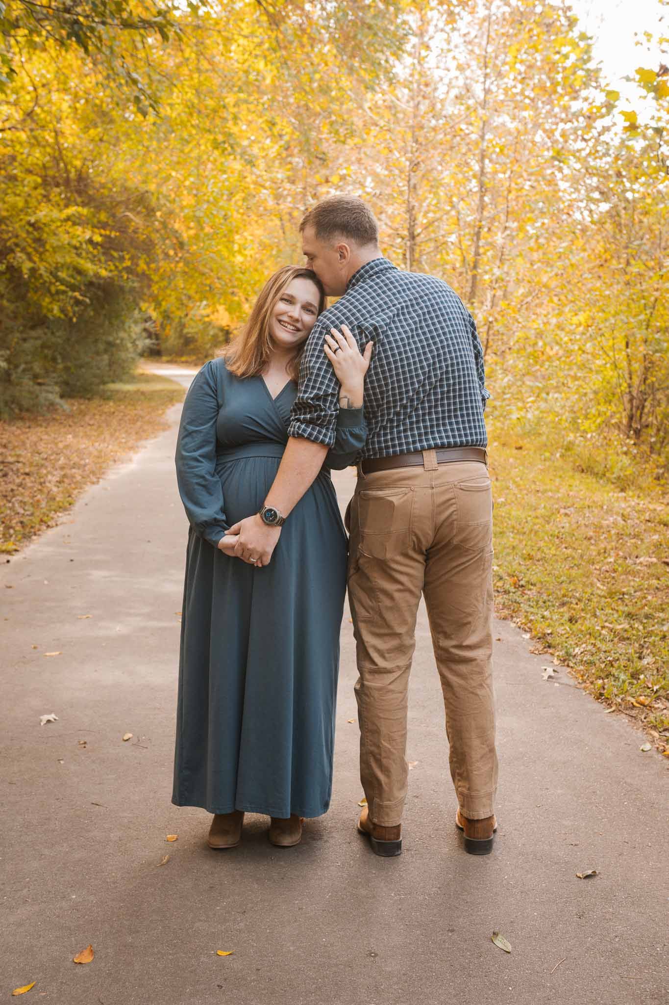 A couple shares tender moments on a tree-lined path surrounded by golden autumn foliage.
