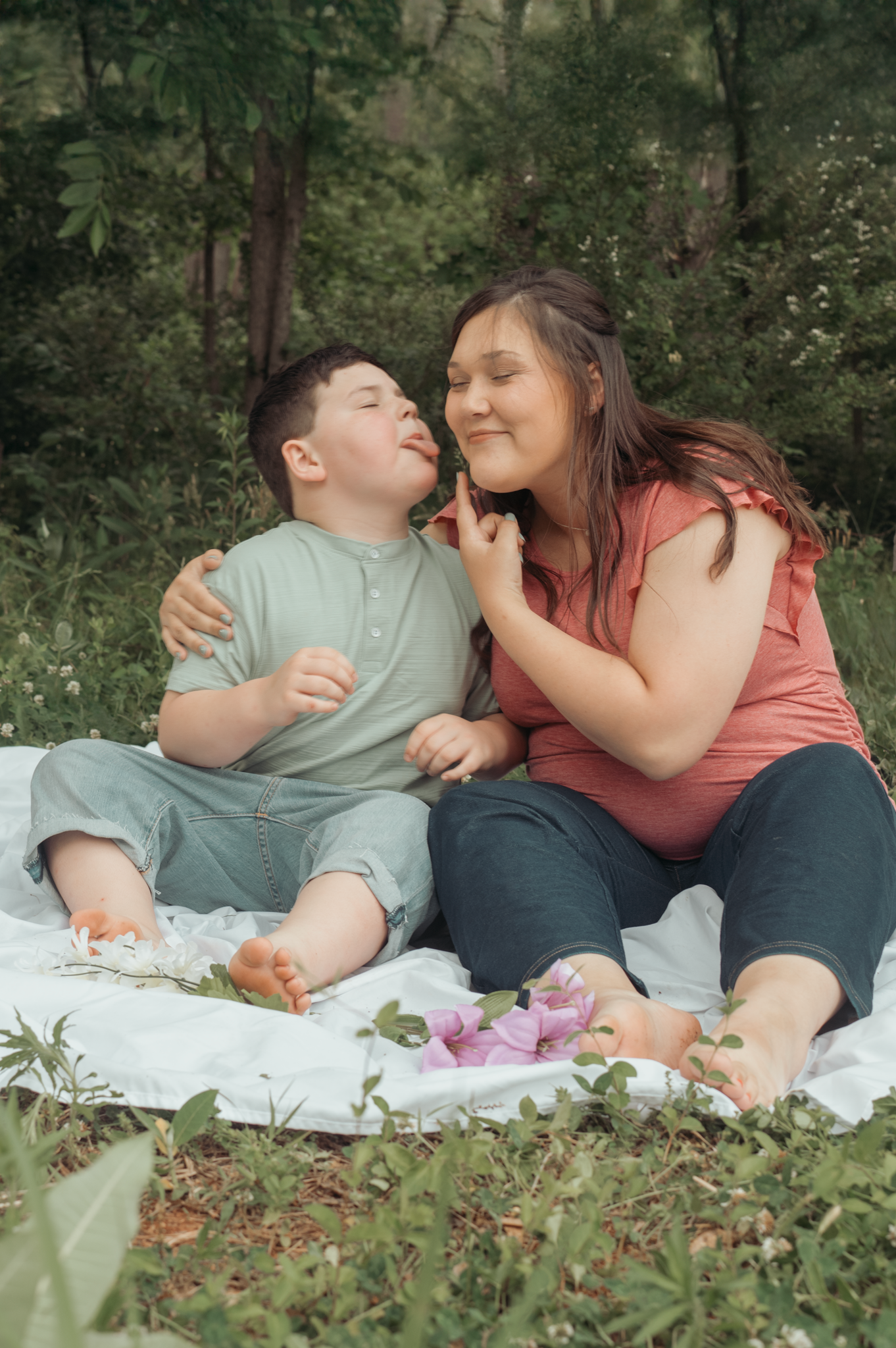 Two people sharing a tender moment while sitting on a white blanket during an outdoor picnic in a wooded setting.