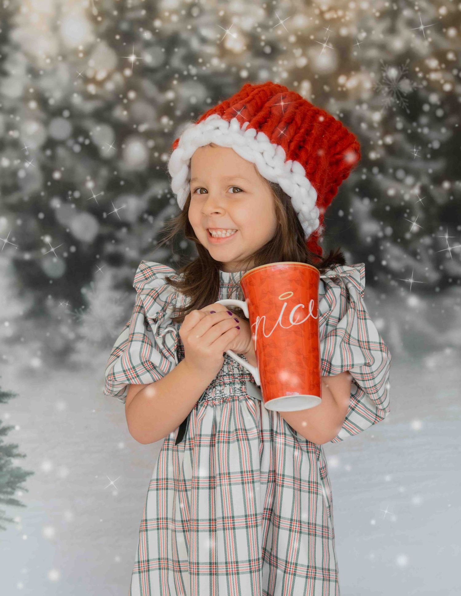 A child in a plaid dress and red Santa hat holds a festive red cup while snow falls in the background.