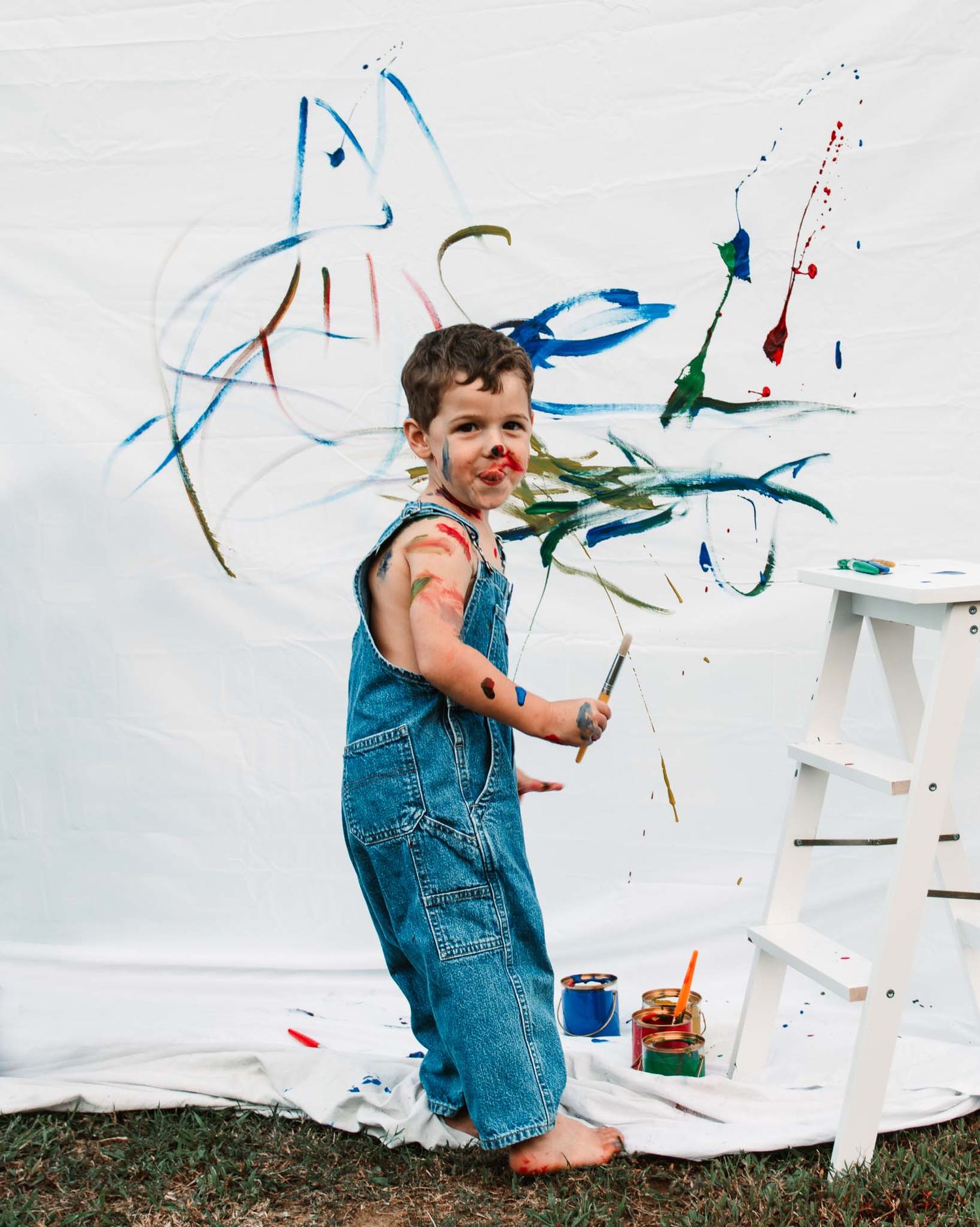 Colorful paint splatters and art supplies surround a creative painting session against a white background.