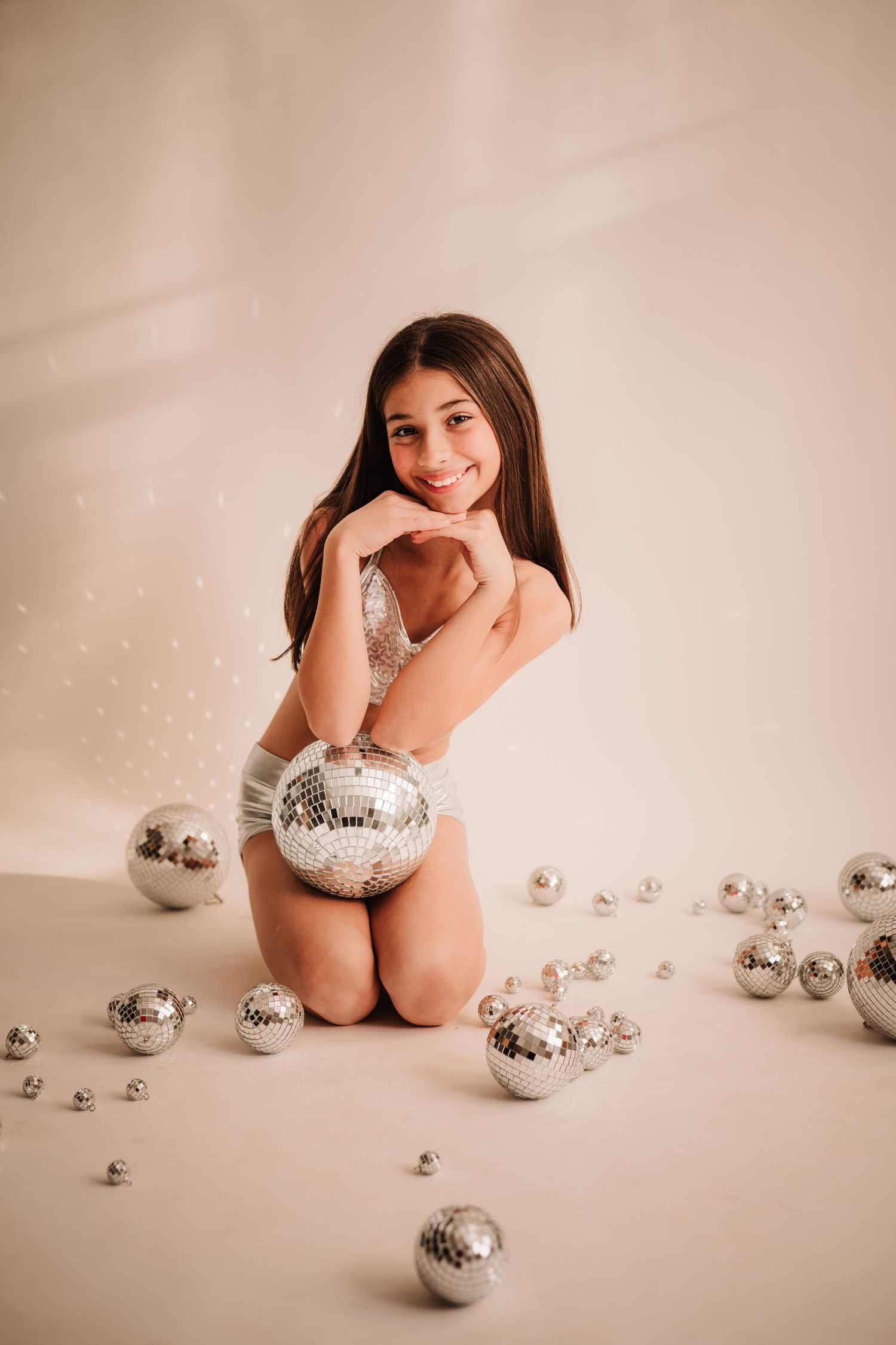 Artistic portrait with silver disco balls scattered on beige background creating festive holiday atmosphere.