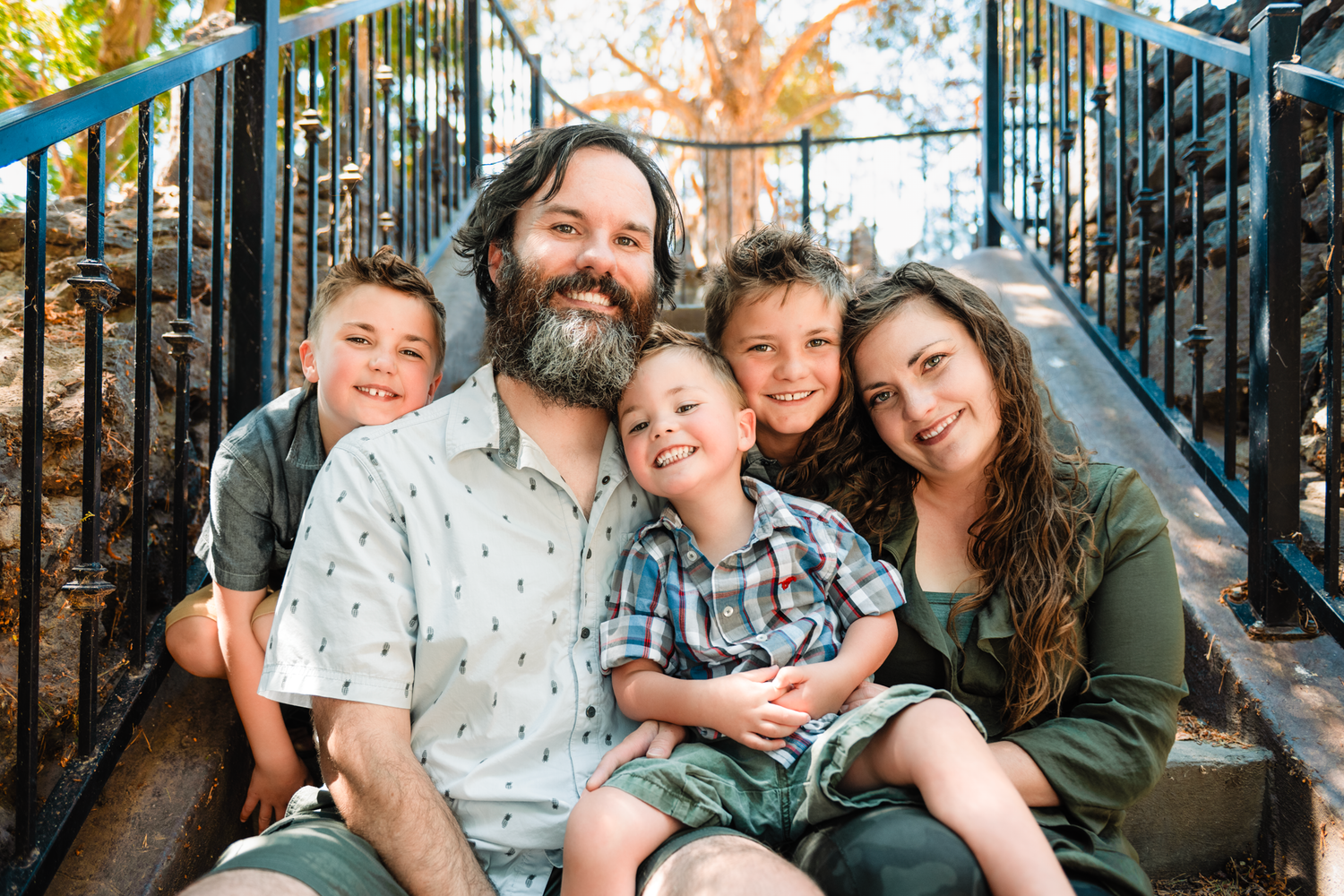 A happy group sits together outdoors on steps during a sunny autumn day with fall foliage in the background.