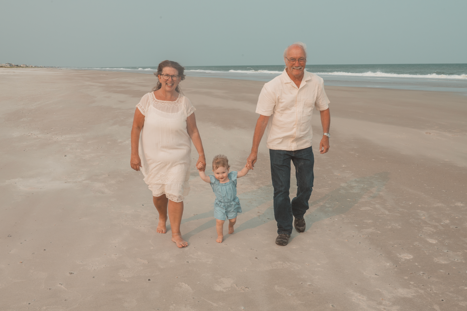 Family of three taking a stroll together on a peaceful beach during an overcast day.