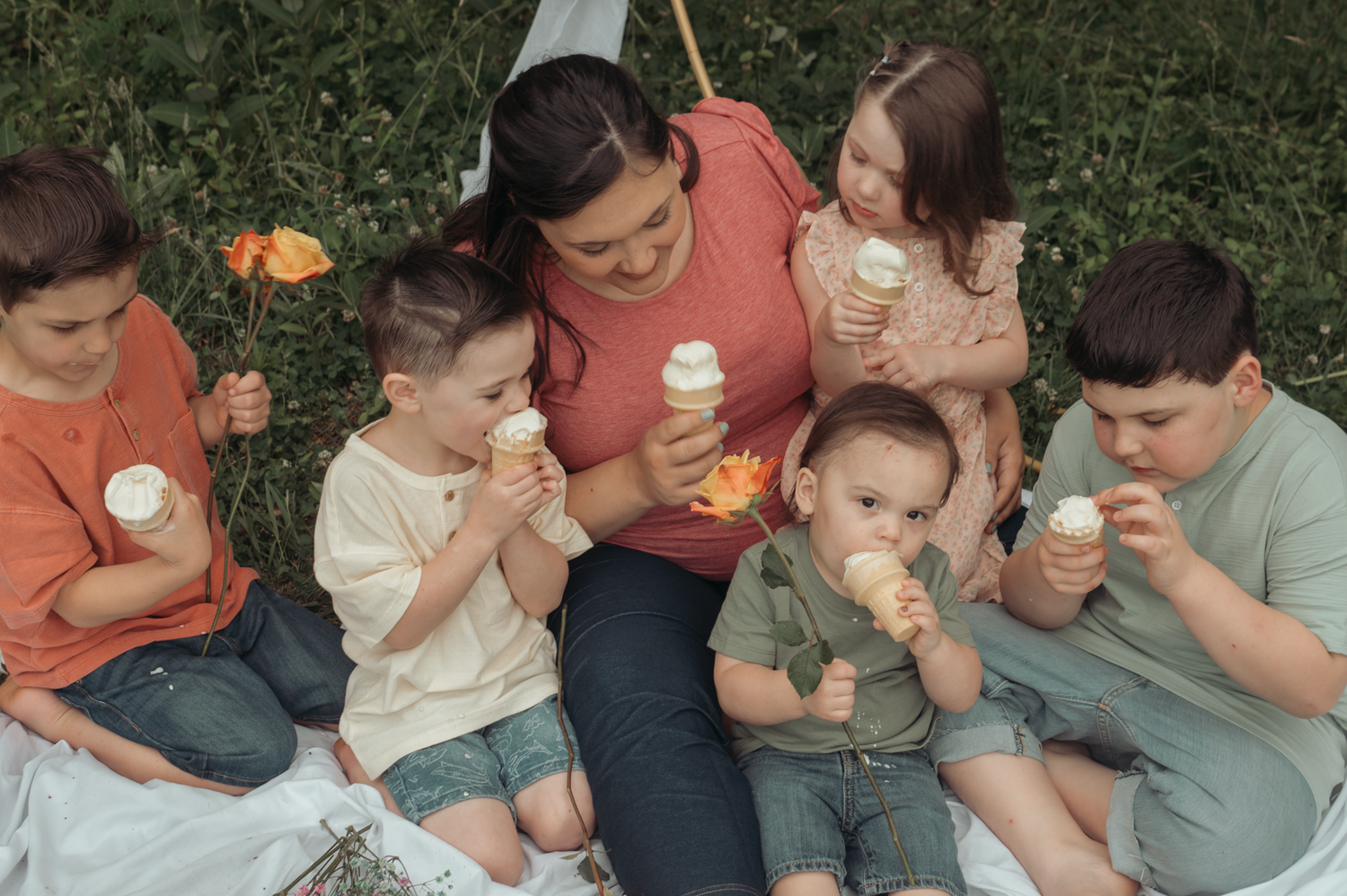 A group enjoying ice cream cones together while sitting on grass during a sunny day outdoors.