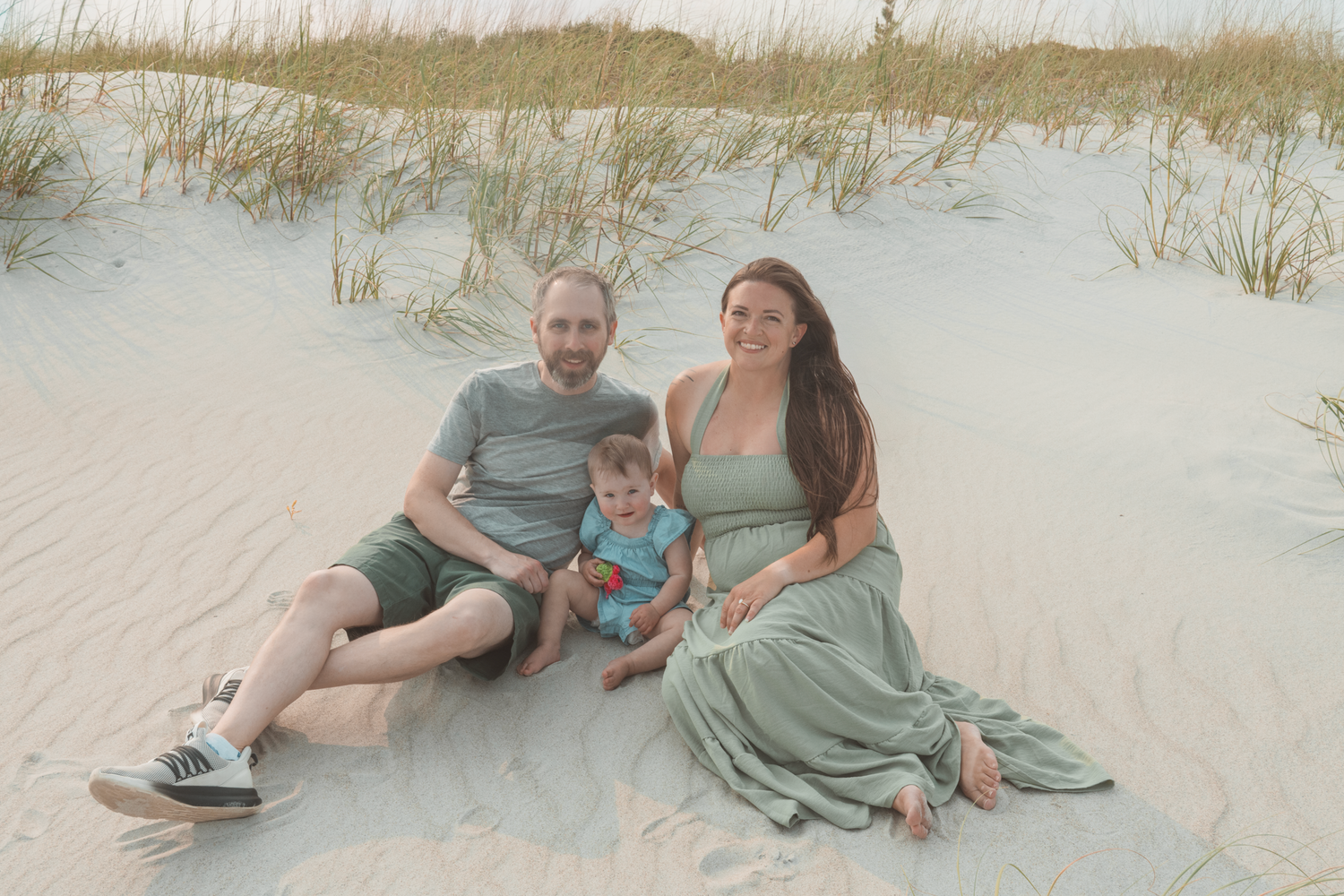 A happy family relaxes together on white sand beach dunes during a warm sunset photo session.