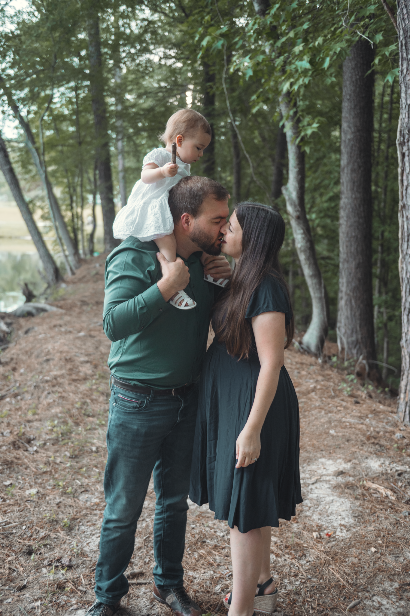 A family of three shares a tender moment together on a wooded forest path.