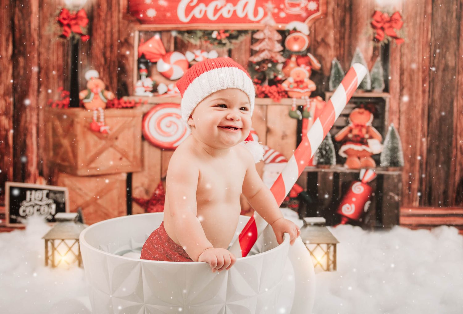 Festive holiday photo with baby in Santa hat sitting in white basket surrounded by red Christmas decorations.