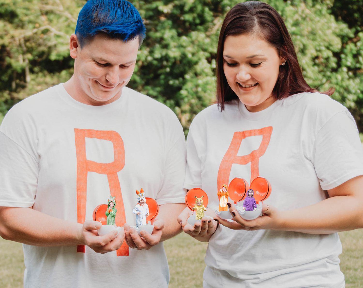 Two people in white t-shirts with orange R letters holding small Pokemon figures outdoors.