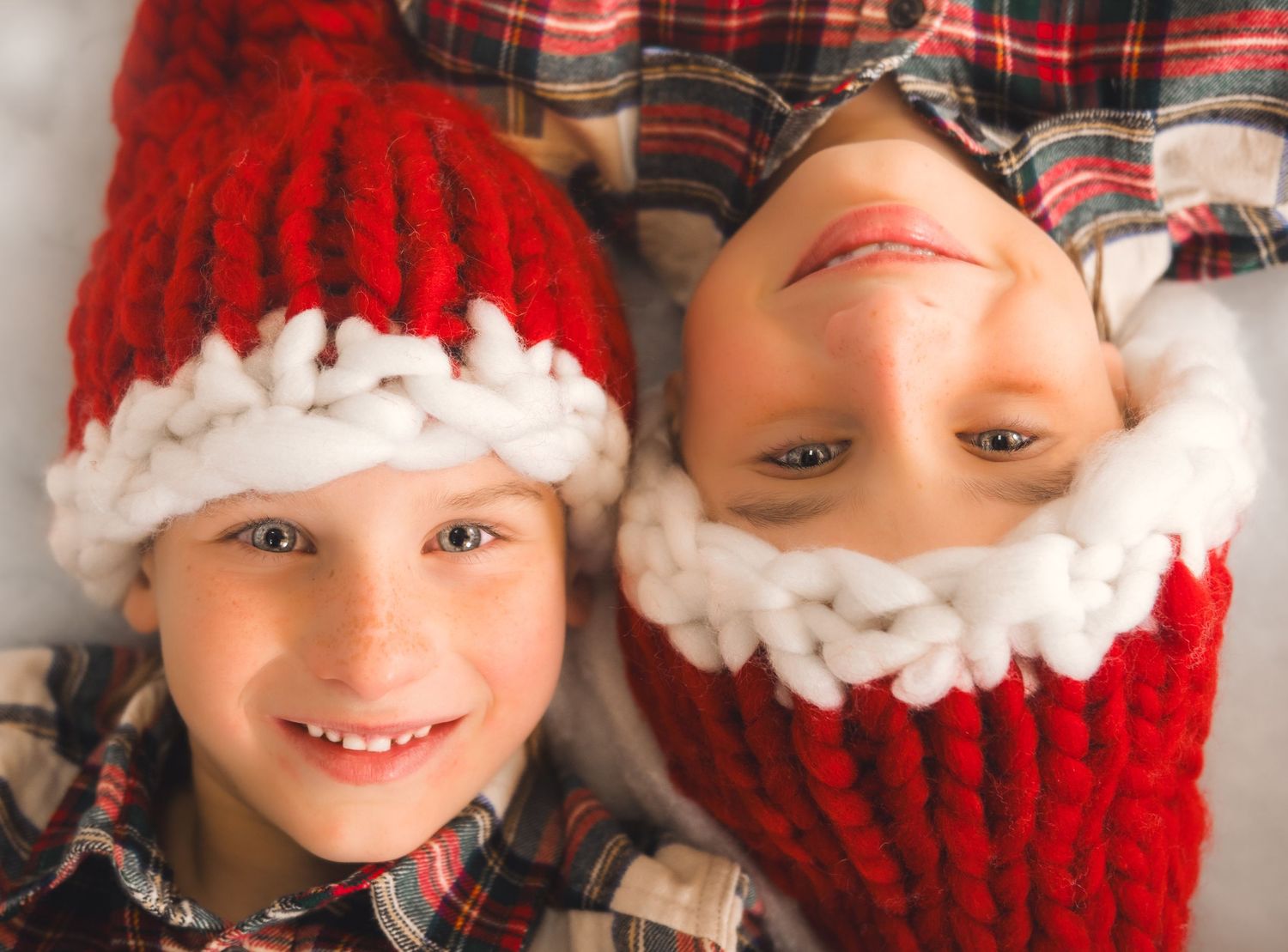 Two people wearing matching red and white knitted winter hats with plaids laying down on the floor.