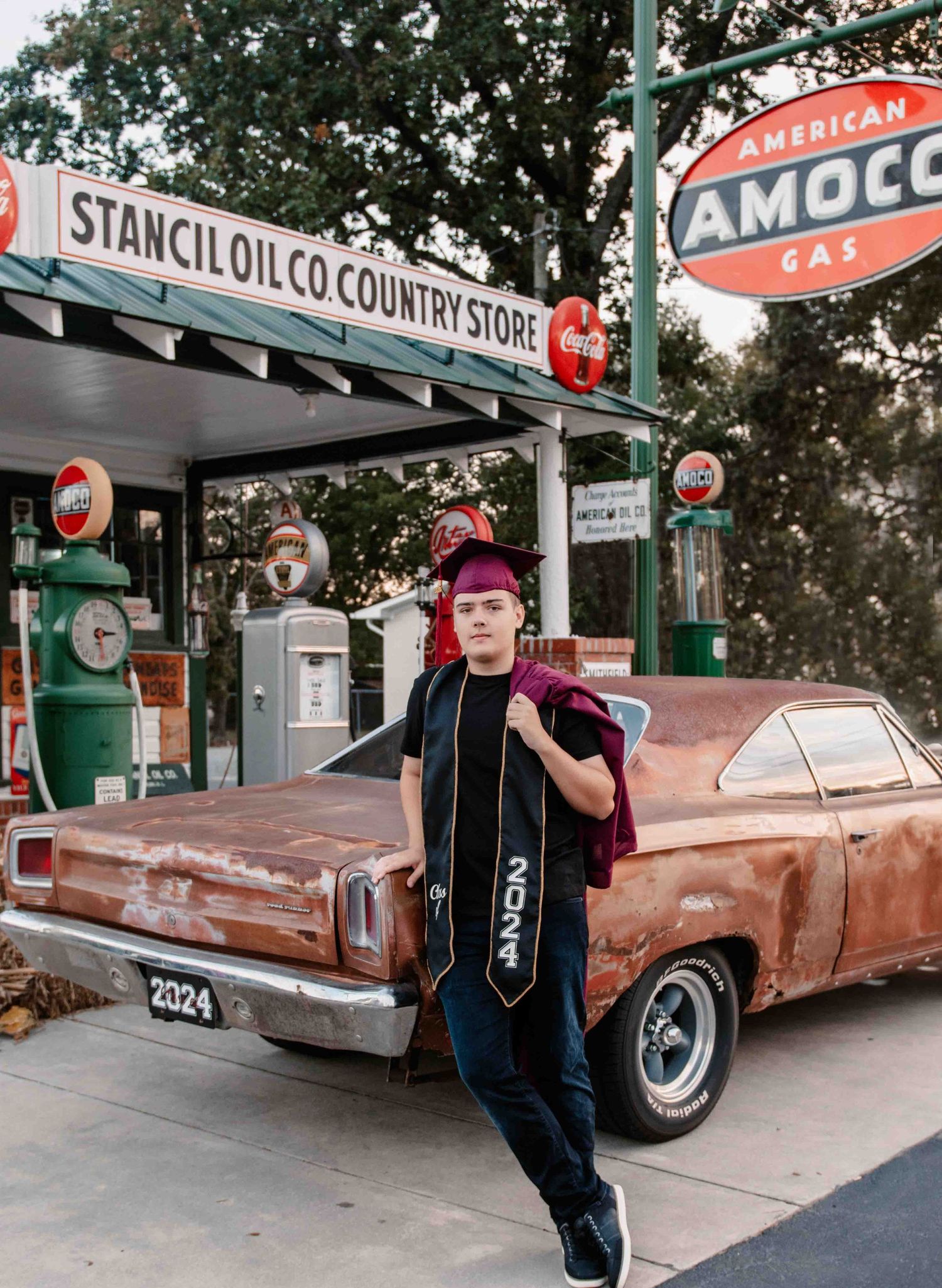 A vintage Amoco gas station with retro pumps and a classic brown car parked under its awning.