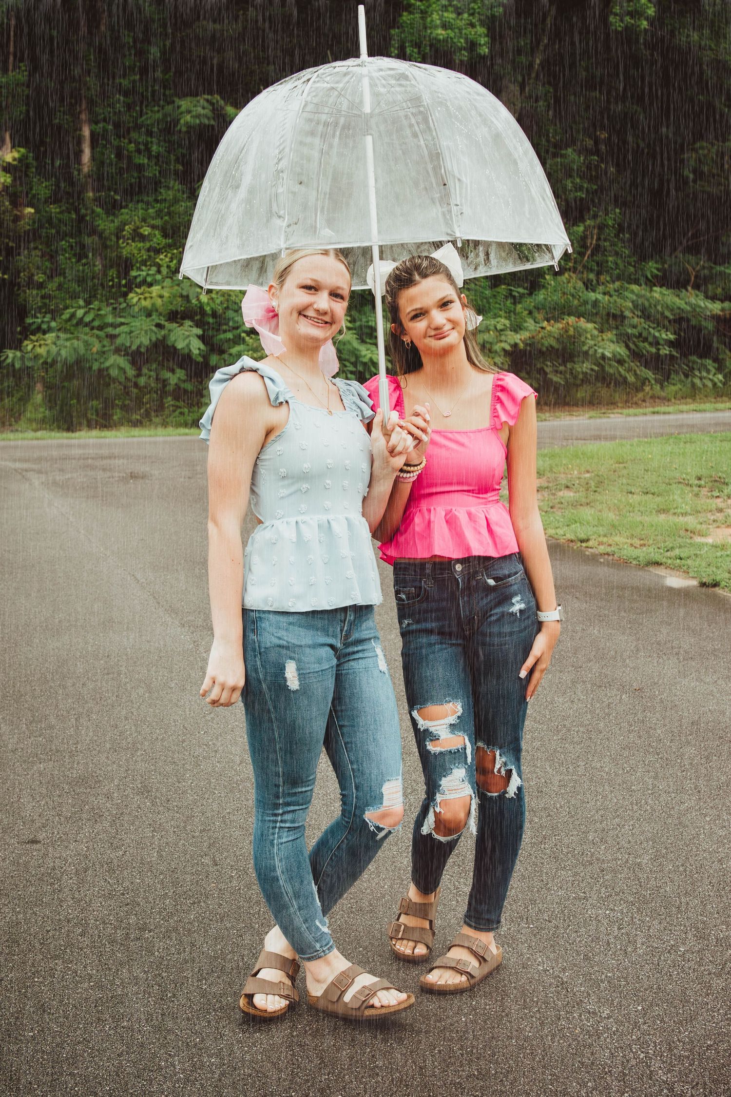 Two young people sharing a clear umbrella in the rain while wearing summer tops, distressed jeans and sandals.