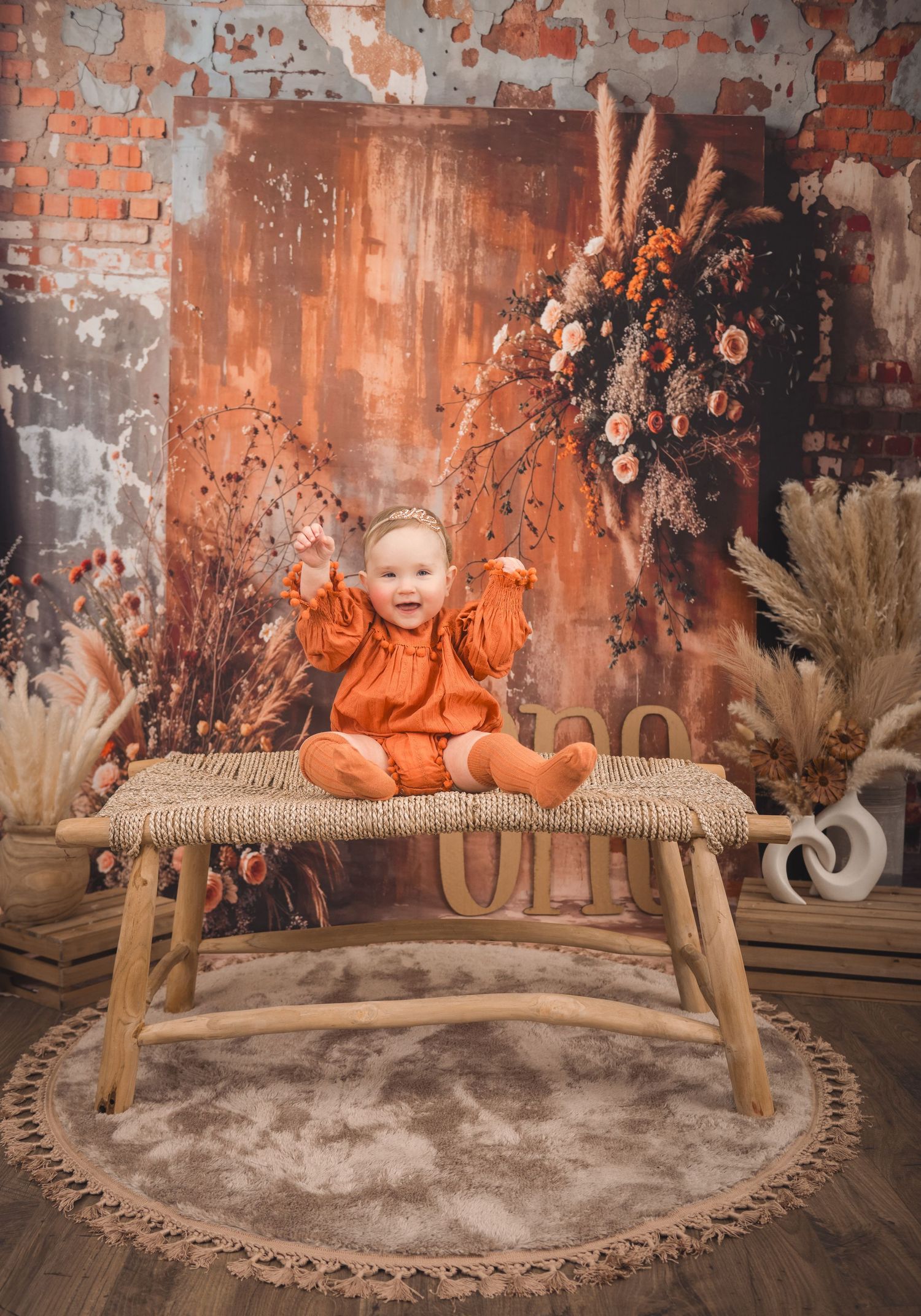 A rustic fall-themed photoshoot setup with dried flowers, wheat stalks, and a wooden bench.