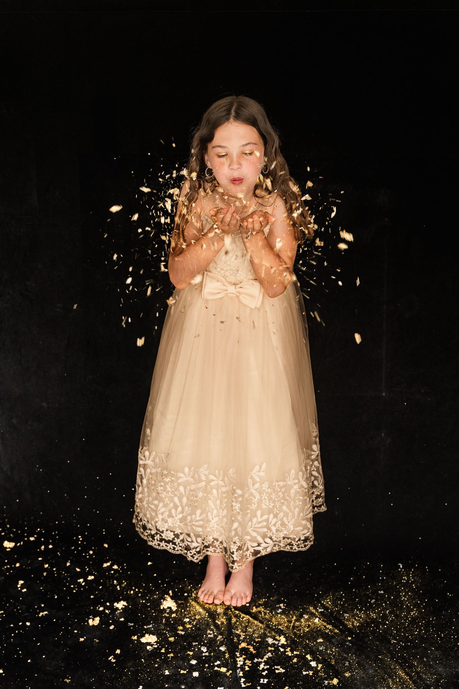 A dreamy night portrait of someone in a cream tulle dress blowing gold glitter in a magical starlit atmosphere.
