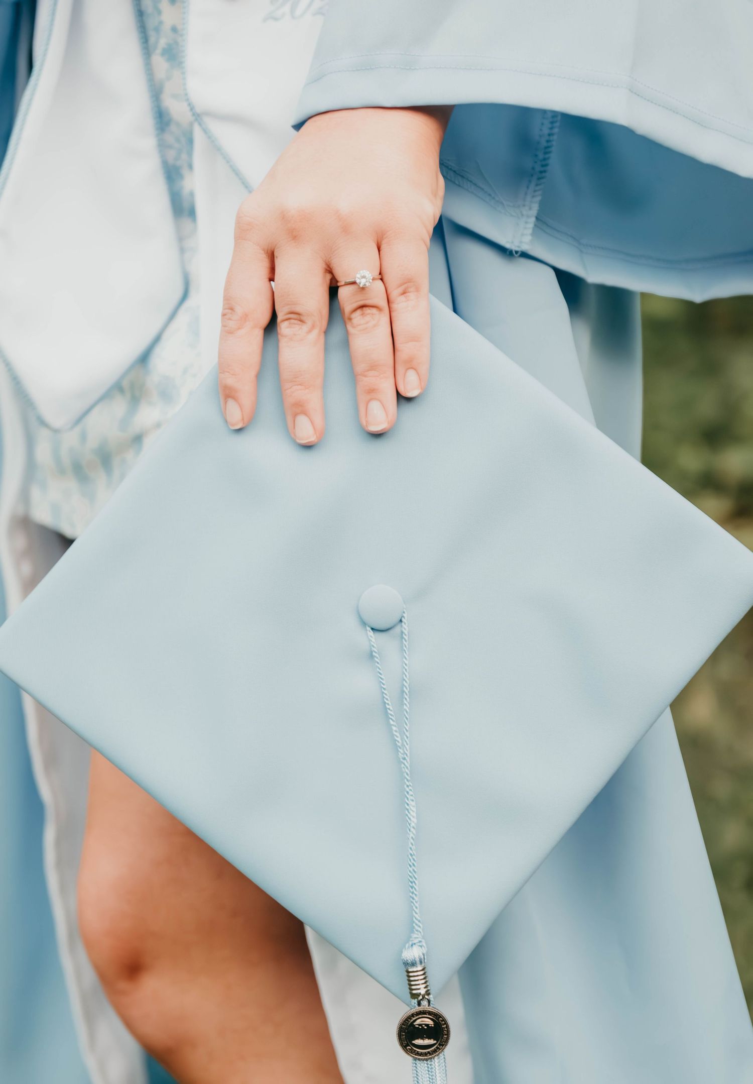 Close-up view of a hand wearing a ring holding a light blue graduation cap with tassel.