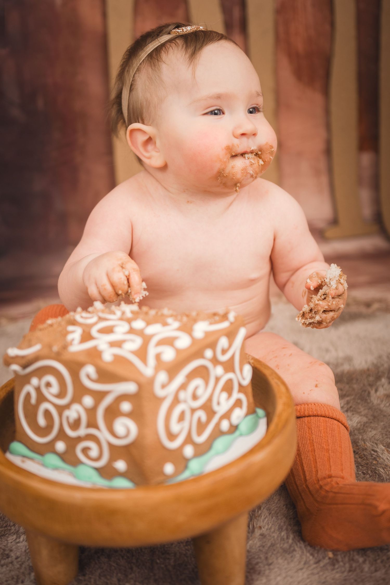 Baby smiling while enjoying her cake smash birthday cake with white frosting patterns, wearing orange socks in Smithfield, NC