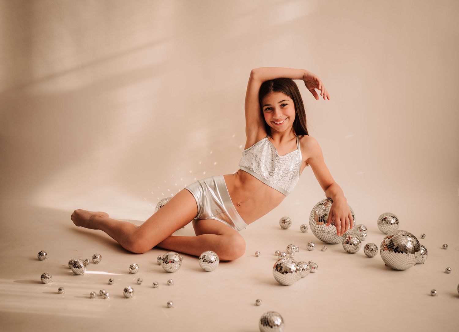 Contemporary dance-inspired studio portrait with scattered silver disco balls and dramatic light against beige backdrop.