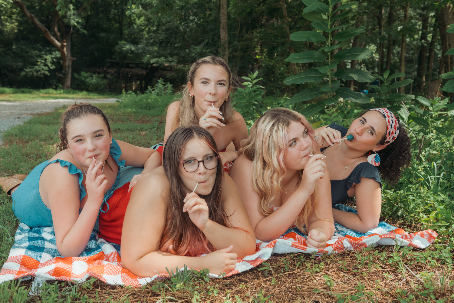 Five friends enjoy popsicles while relaxing together on blankets in a green outdoor setting during summer.