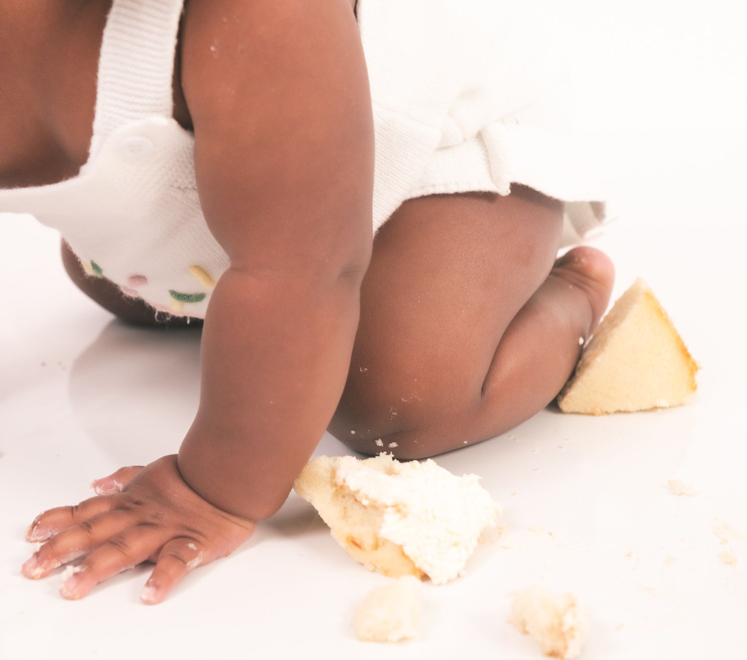 Close-up view of a baby crawling on floor near crumbs and scattered food pieces.