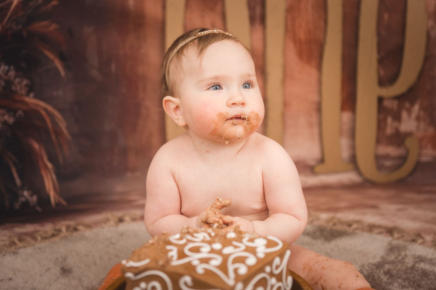 Baby with a smeared face sitting in a cloth-covered seat during a cake smash photo session.