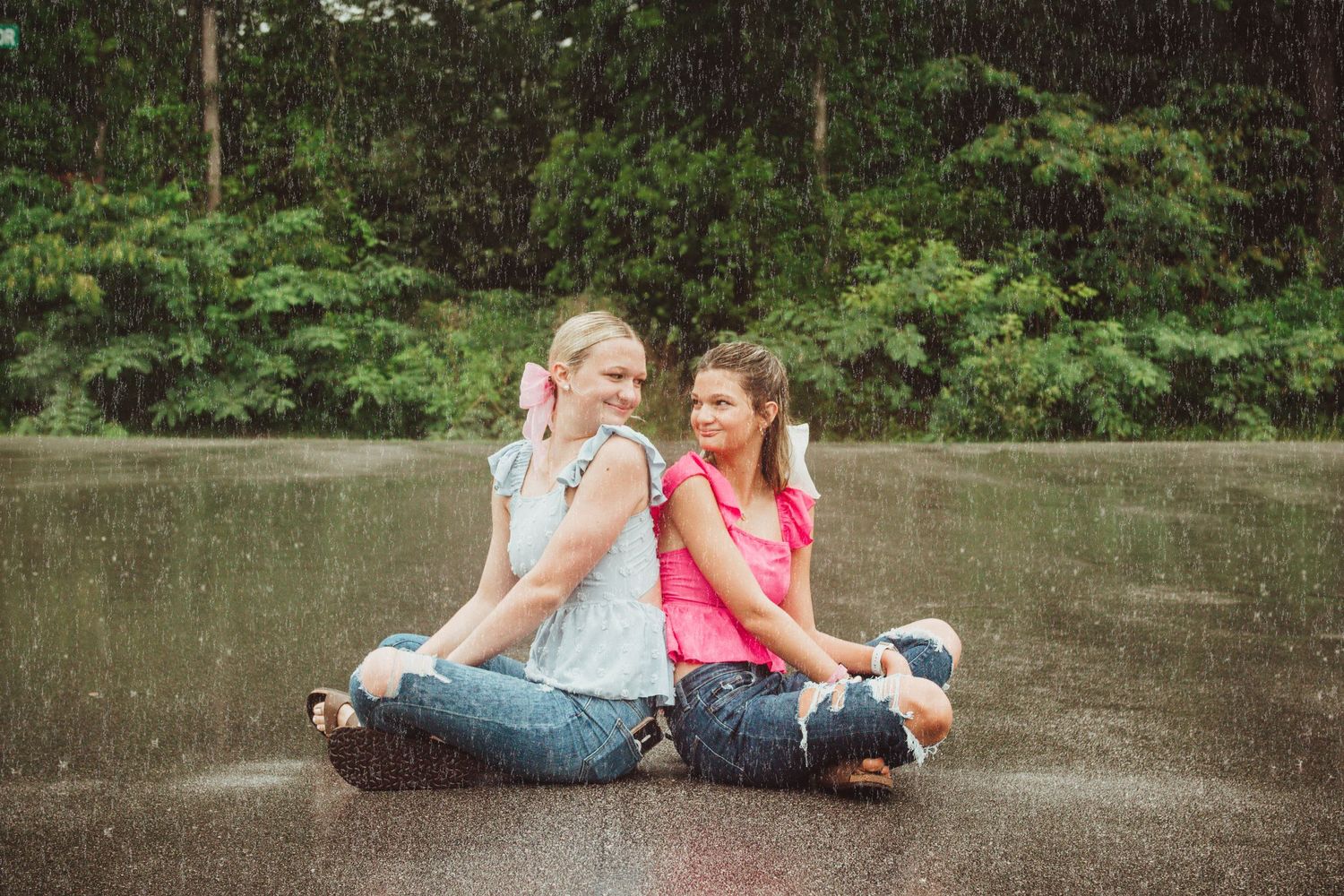 Two people sitting back to back on wet pavement while enjoying ice cream cones on a summer day.