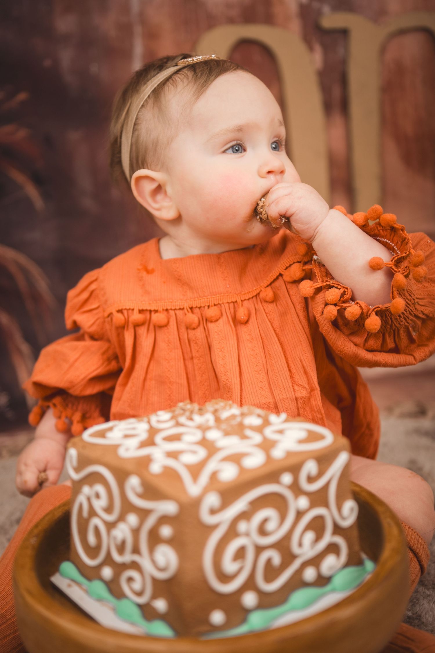 A baby in a frilly orange dress reaches for a chocolate-frosted cake decorated with elegant white swirls in Smithfield, NC - Krystie Nicole