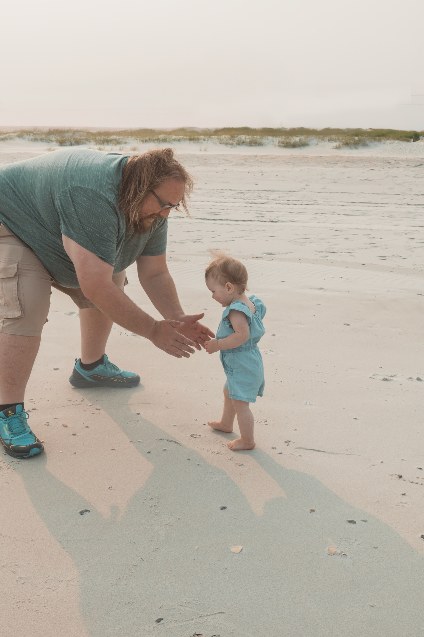 Four sequential beachside photos show an adult and toddler walking together in the sand near ocean dunes.