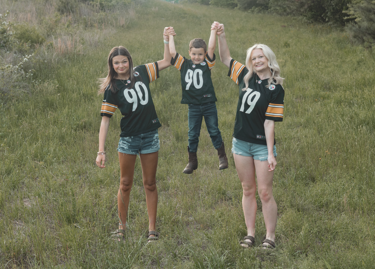 Three people wearing matching jersey numbers 90 and 17 stand in a grassy field with arms raised in celebration.