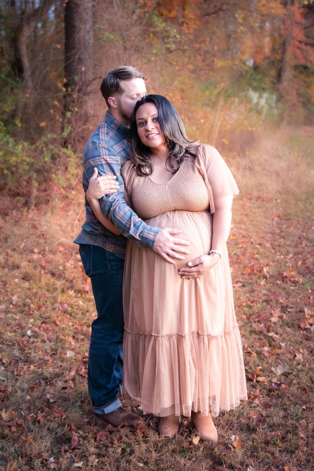 A romantic couple embraces in an autumn forest setting with fallen leaves and warm lighting.