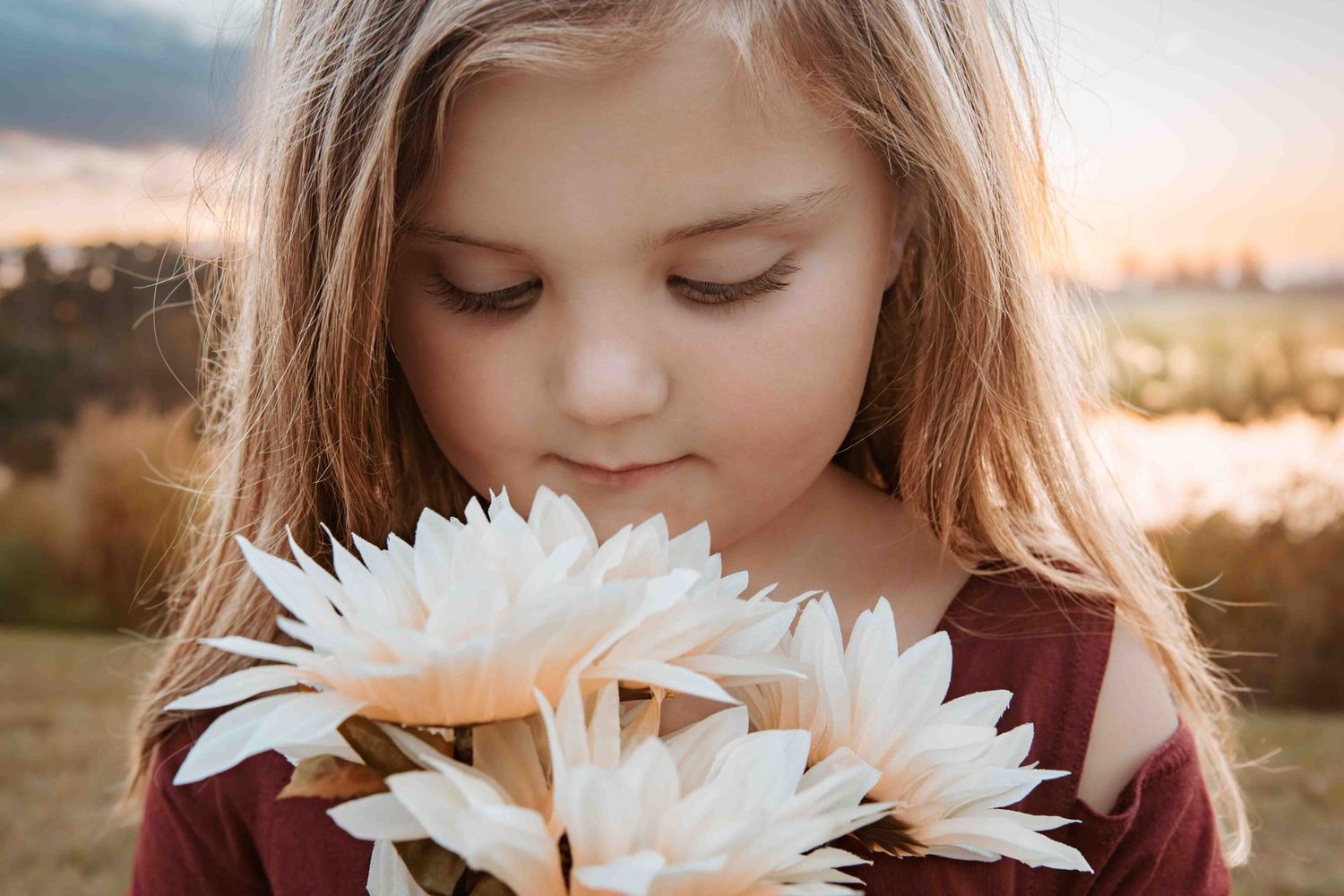 Soft white dahlias frame a gentle downward gaze as golden sunlight illuminates the peaceful outdoor scene.