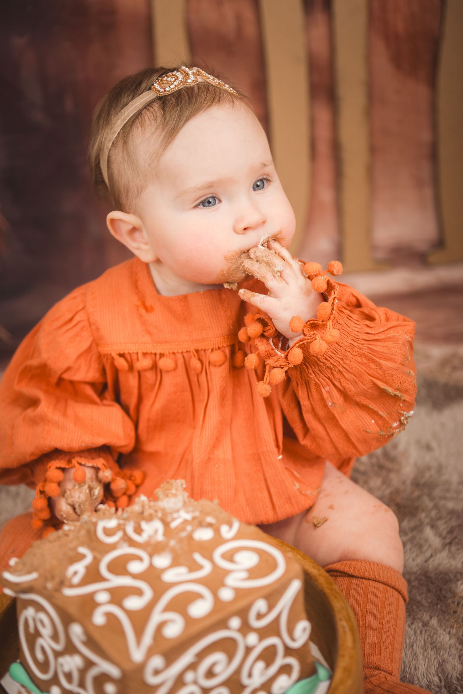 A small child in an orange dress enjoys tasting a beautifully decorated brown cake.