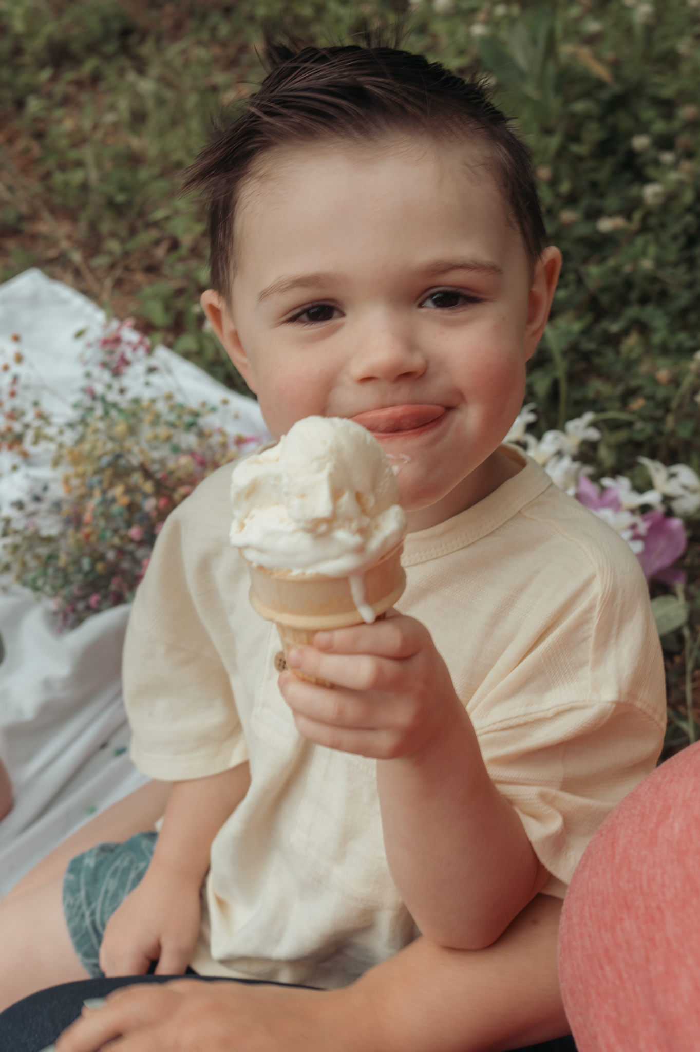 Young child enjoying a vanilla ice cream cone on a sunny day in a garden setting.