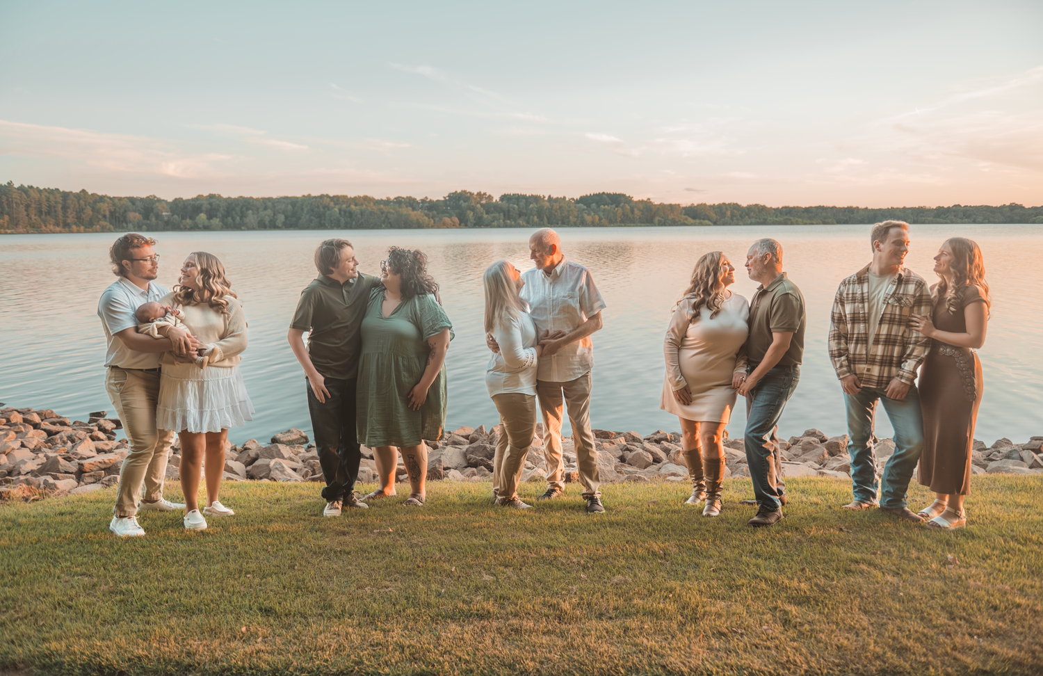 A group of people seen from behind walk together on grassy terrain at sunset near a lake or beach area.