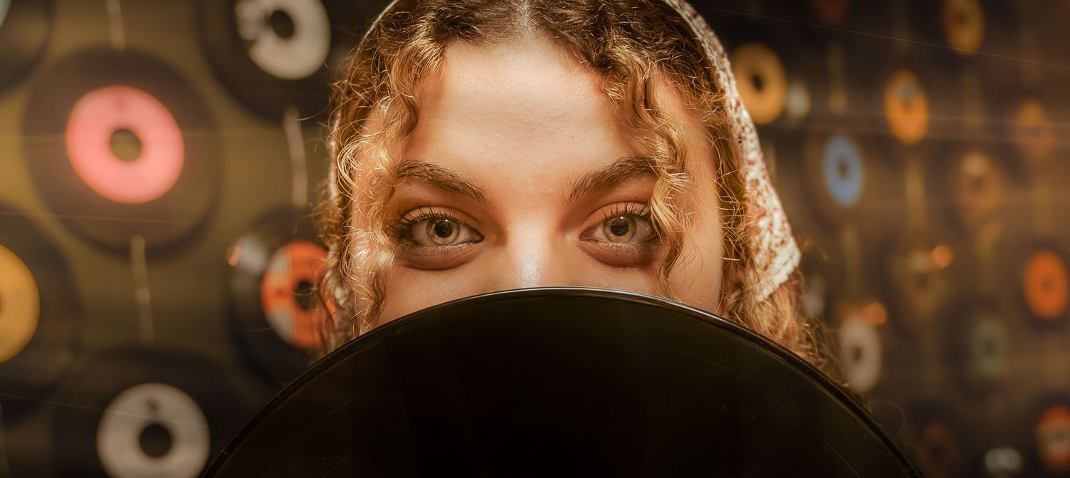 A close-up shot of eyes peering over a dark object with vinyl records blurred in the background.