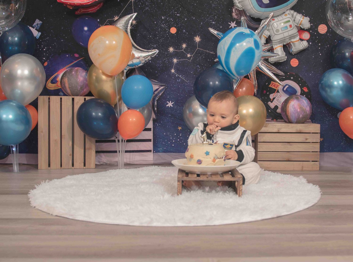 Cake smash session with space party decorations featuring wooden crates and colorful balloons, against a starry background in Smithfield, NC
