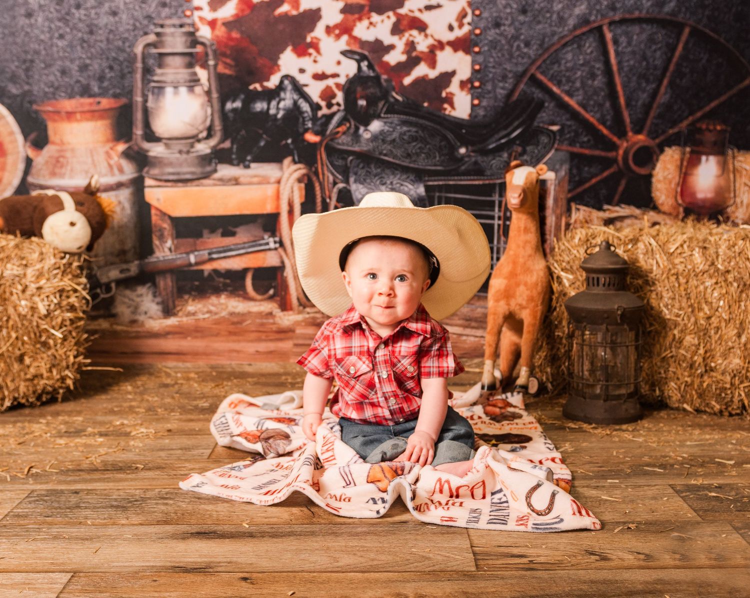 Western themed studio photo set with hay bales, wooden floor, wagon wheel, and rustic decorations in warm lighting.