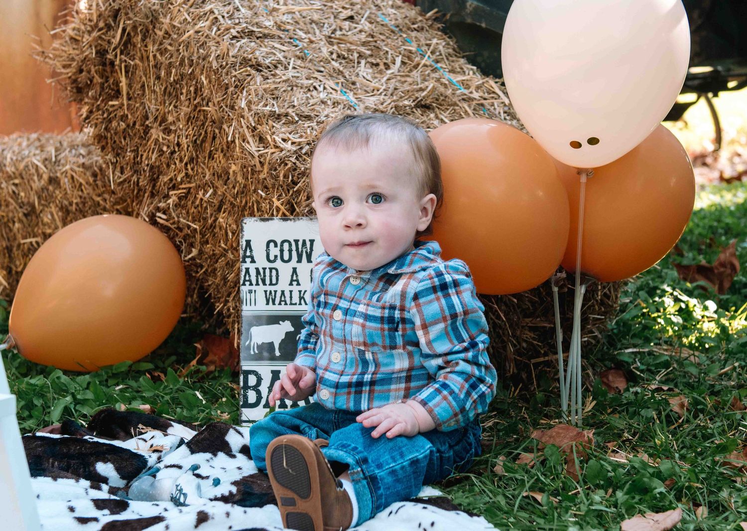 Fall themed baby photo with hay bales, orange balloons, and rustic country decor in an outdoor setting.