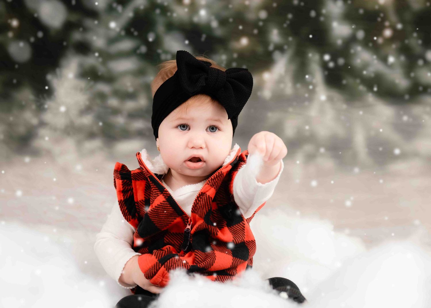 Small child in buffalo plaid coat and black bow hat reaches up during winter snow scene.