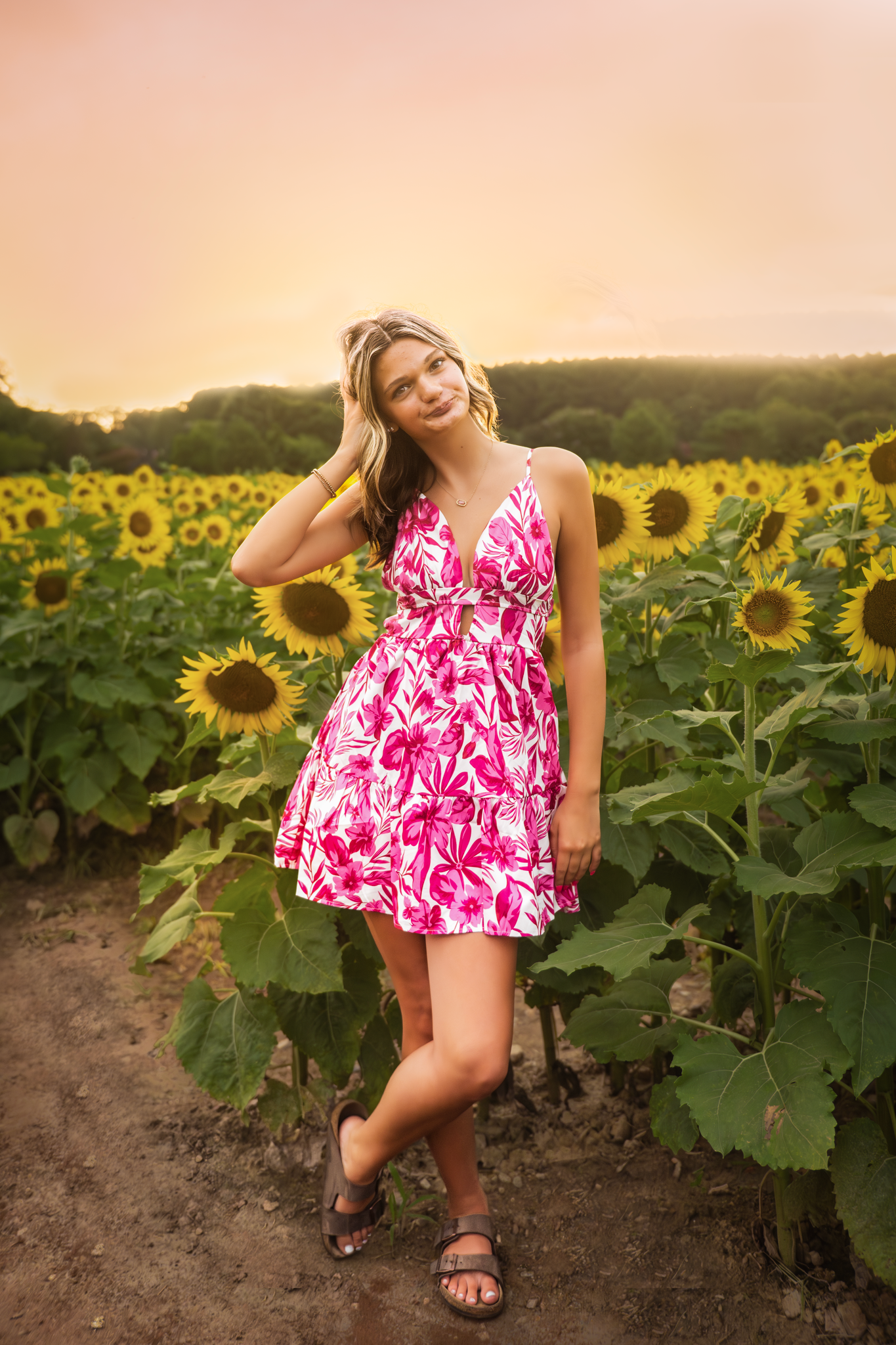 A pink floral summer dress stands out against a beautiful sunflower field at sunset, creating a dreamy outdoor portrait.